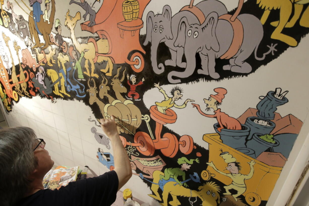 John Simpson, project director of exhibitions for The Amazing World of Dr. Seuss Museum, paints a mural based on artwork in the Dr. Seuss book “Did I Ever Tell You How Lucky You Are?” on a wall at the museum, in Springfield, Mass.