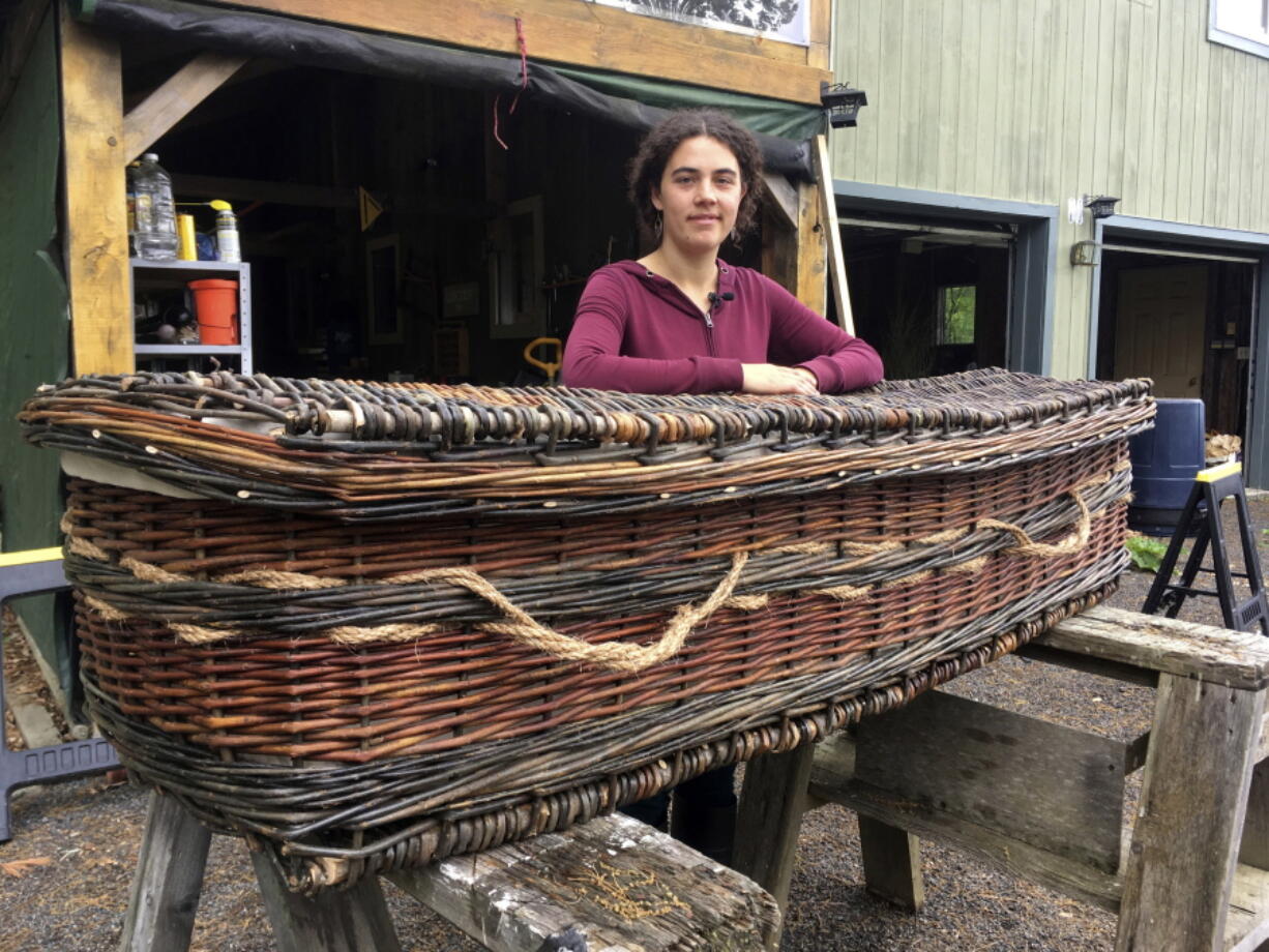 In this May 24, 2017, photo, Mary Lauren Fraser stands beside a casket she hand-wove from willow, in Montague, Mass. Fraser sells biodegradable, hand-woven urns and caskets for use in green burials. Green burials can save consumers money, and have nurtured a market for biodegradable urns and coffins.