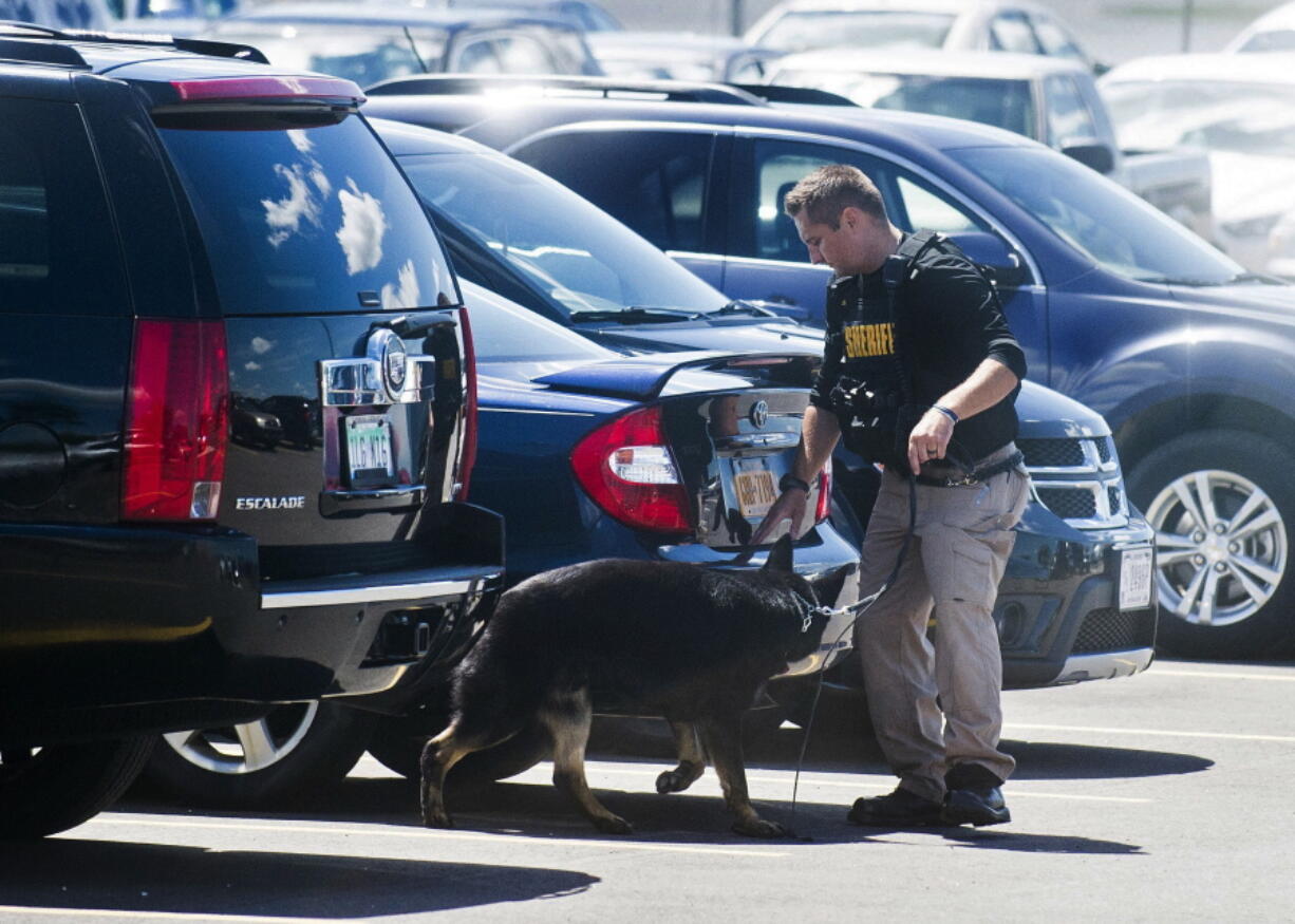 A police dog and handler search cars Wednesday morning in a parking lot at Bishop International Airport in Flint, Mich. Officials evacuated the airport Wednesday after a Canadian man stabbed a police officer in the neck, federal officials said.