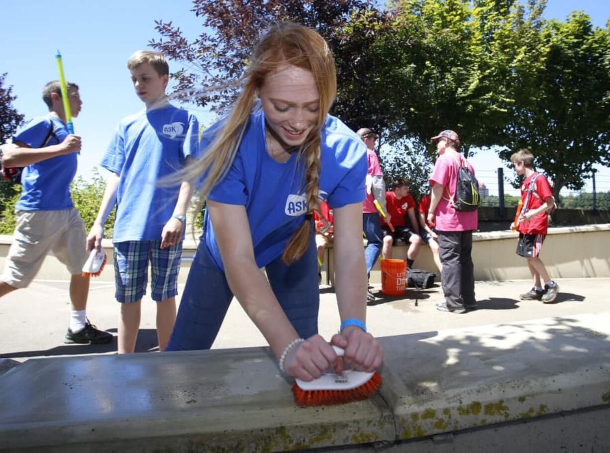 Volunteer Summer Fulcher, 16, of Vancouver, scrubs moss from the Vancouver Land Bridge Saturday as part of “The Amazing Race Youth Conference.”