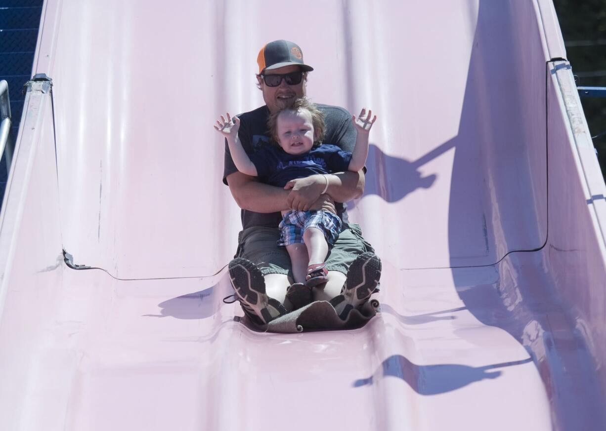 Gerard Nash and his son, Radley, 2 ride a slide at a carnival as part of Battle Ground Harvest Days on Saturday.