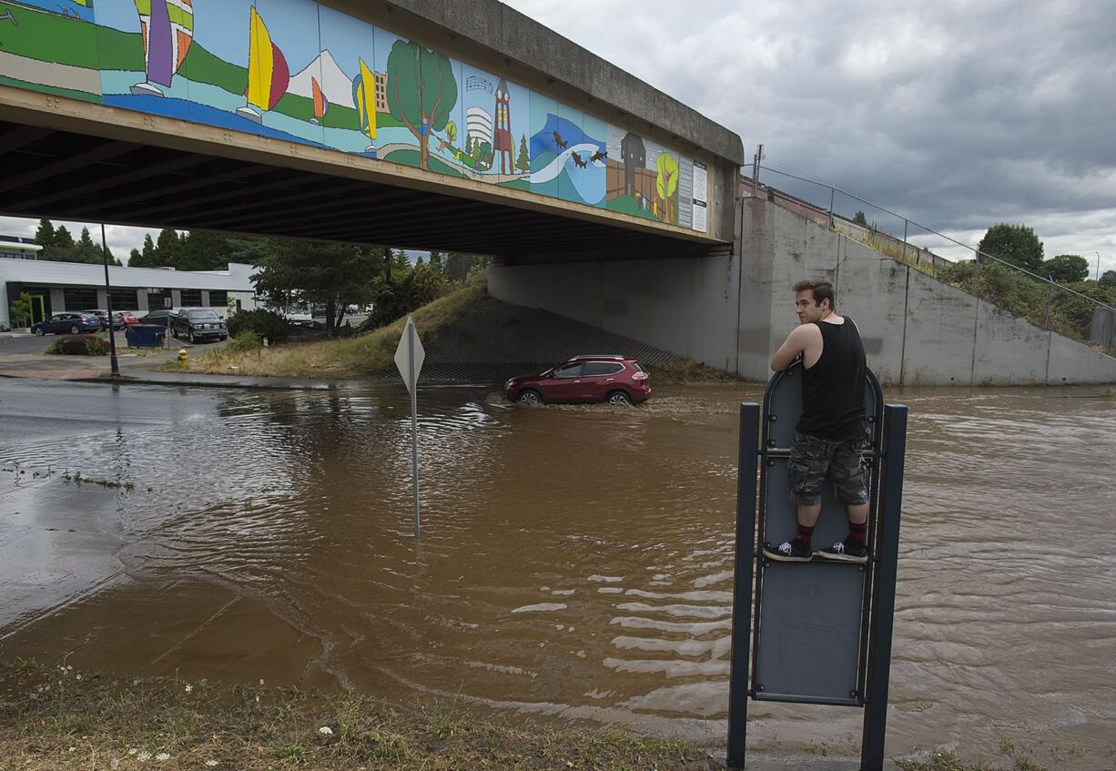 A motorist navigates standing water on Columbia Street after a water main break as George Janzen of Vancouver checks out the scene Thursday afternoon, July 20, 2017.