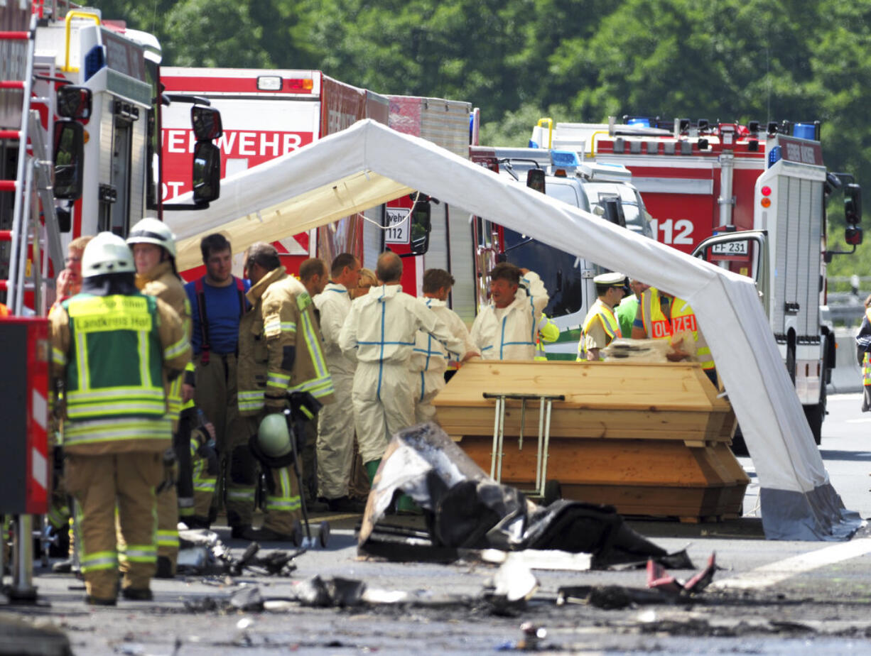 Police and rescuers stand near coffins on the motorway A9 near Muenchberg, Germany, Monday, July 3, 2017. Several people are feared dead after a bus carrying a group of German senior citizens crashed into a truck on a highway in Bavaria early Monday and burst into flames, police said.