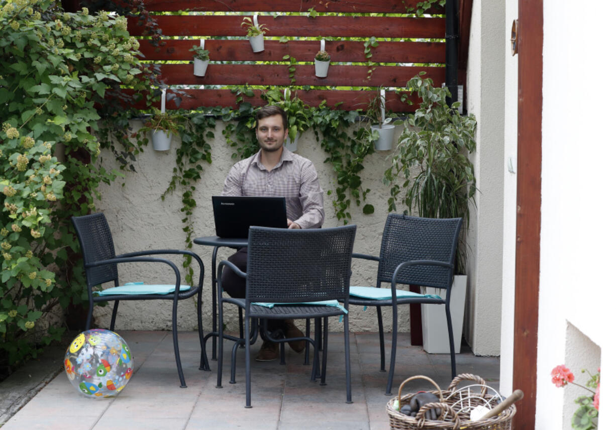 In this Tuesday, July 25, 2017, photo, Vilem Prochazka, an employee of Boston-based software company KangoGift, poses for a photo while sitting with his laptop in his garden, at his home in Kolin, Czech Republic. At some small businesses, the traditional chat around the watercooler takes place online and meetings are held via Skype, as staffers are working at home.