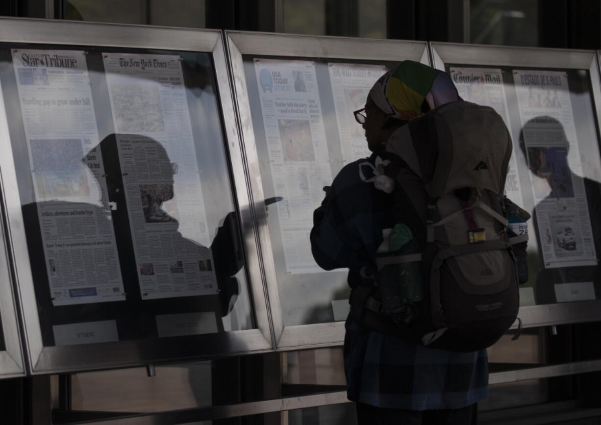 A woman, who did not wish to give her name, reads newspaper front pages displayed at the Newseum in Washington, Monday, July 10, 2017. News outlets are seeking permission from Congress for the right to negotiate jointly with Google and Facebook, two companies that dominate online advertising and online news traffic.