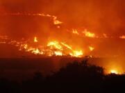 A wildfire burns on a hillside above stopped railcars near Othello on Aug. 13. The fire is one of many in the region that helped deplete fire fighting resources. (AP Photo/Ted S.