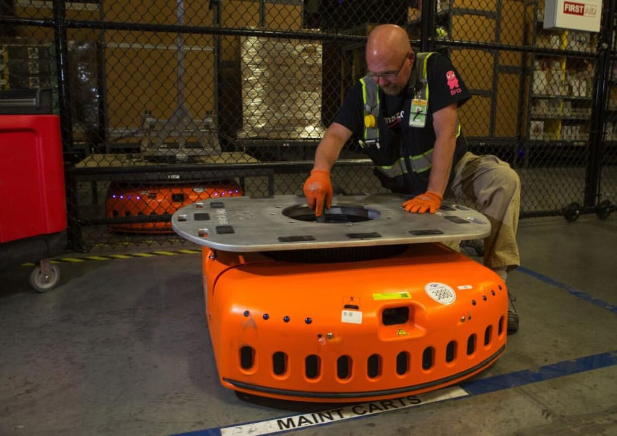 Barry Tormoehlen, a maintenance technician at Amazon’s fulfillment center in DuPont, vacuums the inside of a KIVA, one of Amazon’s robots that are used to move items around the center July 3. The KIVAs weigh 800 pounds each and can carry up to 3,000 pounds of merchandise. Ellen M.