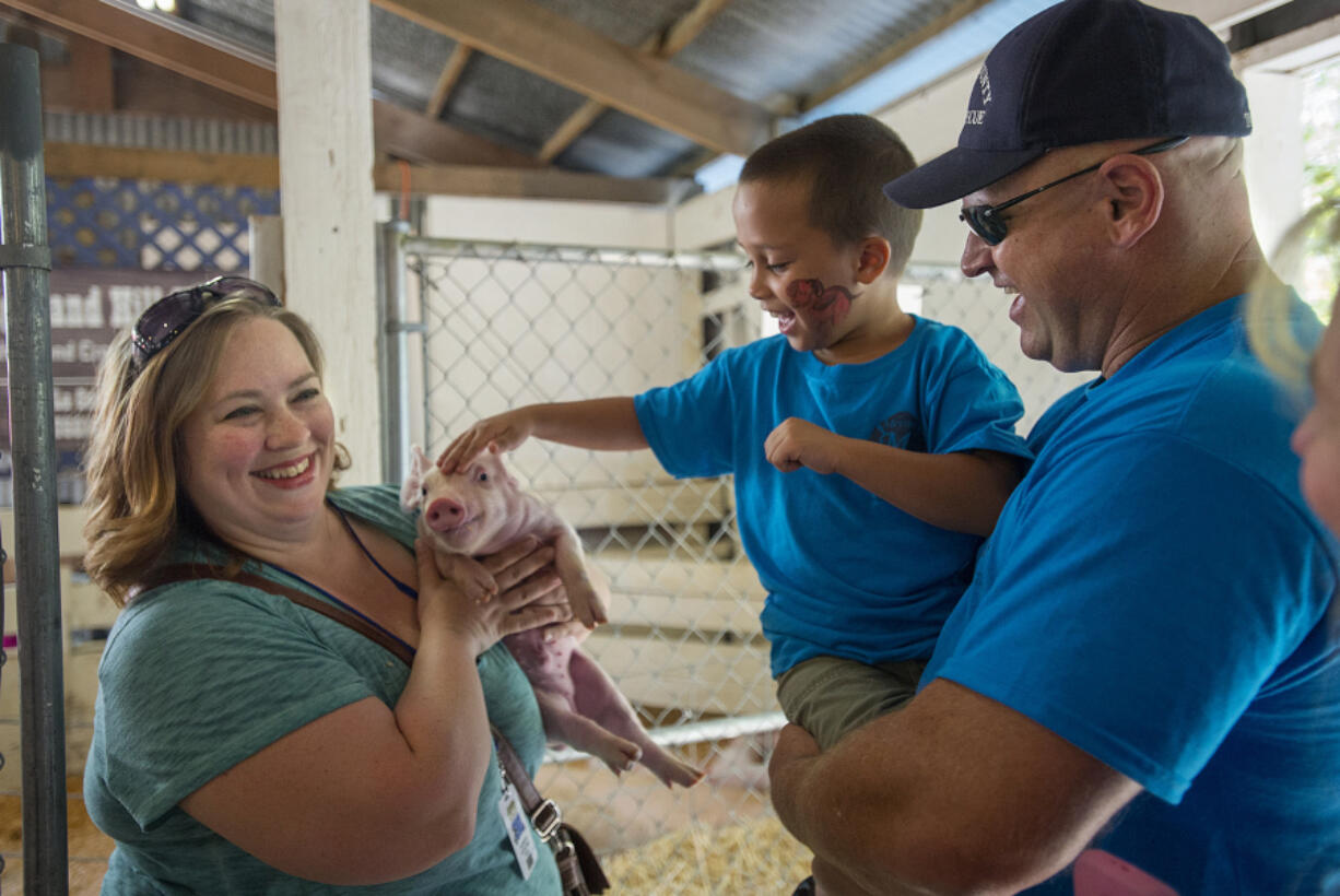 Jodi Ballard of Highland Hill Hogs, from left, introduces a piglet Monday morning to Gabriel Romero, 7, and Capt. Scott Taube of Clark County Fire District 6, who is a member of Memory Makers, at the Clark County Event Center at the Fairgrounds in Ridgefield. The Memory Makers provide support to medically fragile kids so they and their family can enjoy the fair.