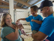 Jodi Ballard of Highland Hill Hogs, from left, introduces a piglet Monday morning to Gabriel Romero, 7, and Capt. Scott Taube of Clark County Fire District 6, who is a member of Memory Makers, at the Clark County Event Center at the Fairgrounds in Ridgefield. The Memory Makers provide support to medically fragile kids so they and their family can enjoy the fair.