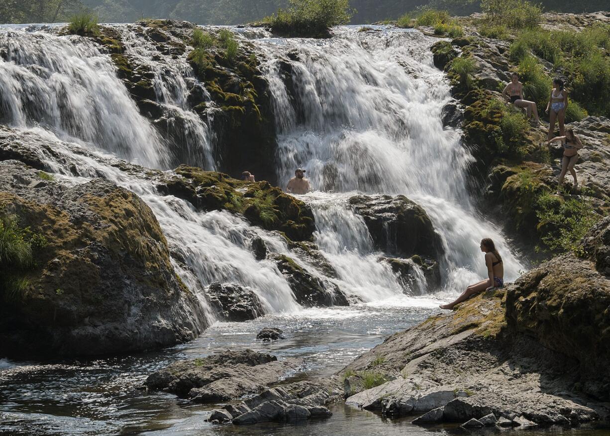 Ellie Lepley of Michigan, foreground right, stretches out on a rock at Dougan Falls while joining a handful of swimmers as they beat the heat northeast of Washougal in Skamania County on Wednesday afternoon, Aug. 2, 2017. Lepley was among the visitors and locals who ventured out into local swimming holes as temperatures were forecast to approach 100 degrees Wednesday.