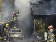 A Vancouver firefighter stands on top of a car in an attempt to put out a fire sparked by a malfunctioning battery charger. The fire destroyed one house and severely damaged a second on East Reserve Street in Vancouver.