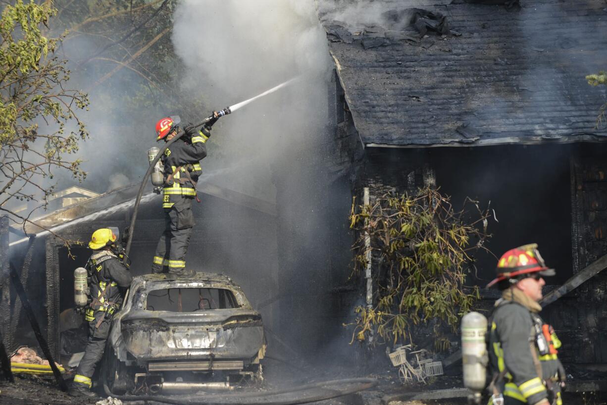 A Vancouver firefighter stands on top a car in an attempt to put out a fire that may have started from a jump-started car battery on East Reserve Street in Vancouver, Thursday August 3, 2017.