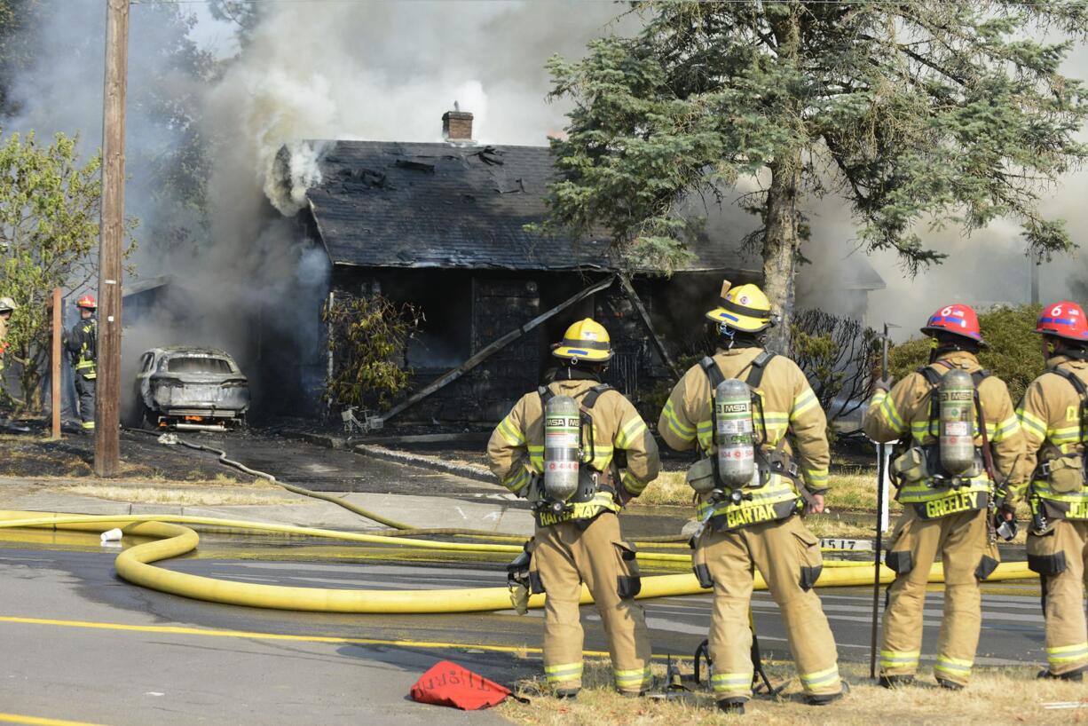 Firefighters watch as crews work to put out a fire that damaged a house, a detached garage and a car, and damaged a second house on East Reserve Street in Vancouver, Thursday August 3, 2017.