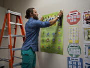 Kyle Sharpe of Vancouver sets up a poster outlining his class’s social curriculum in his new classroom at Chinook Elementary School in Vancouver. An innovative partnership enabled Sharpe to earn his teaching certificate while working as a paraeducator for Vancouver Public Schools and attending classes at the Vancouver campus of City University.