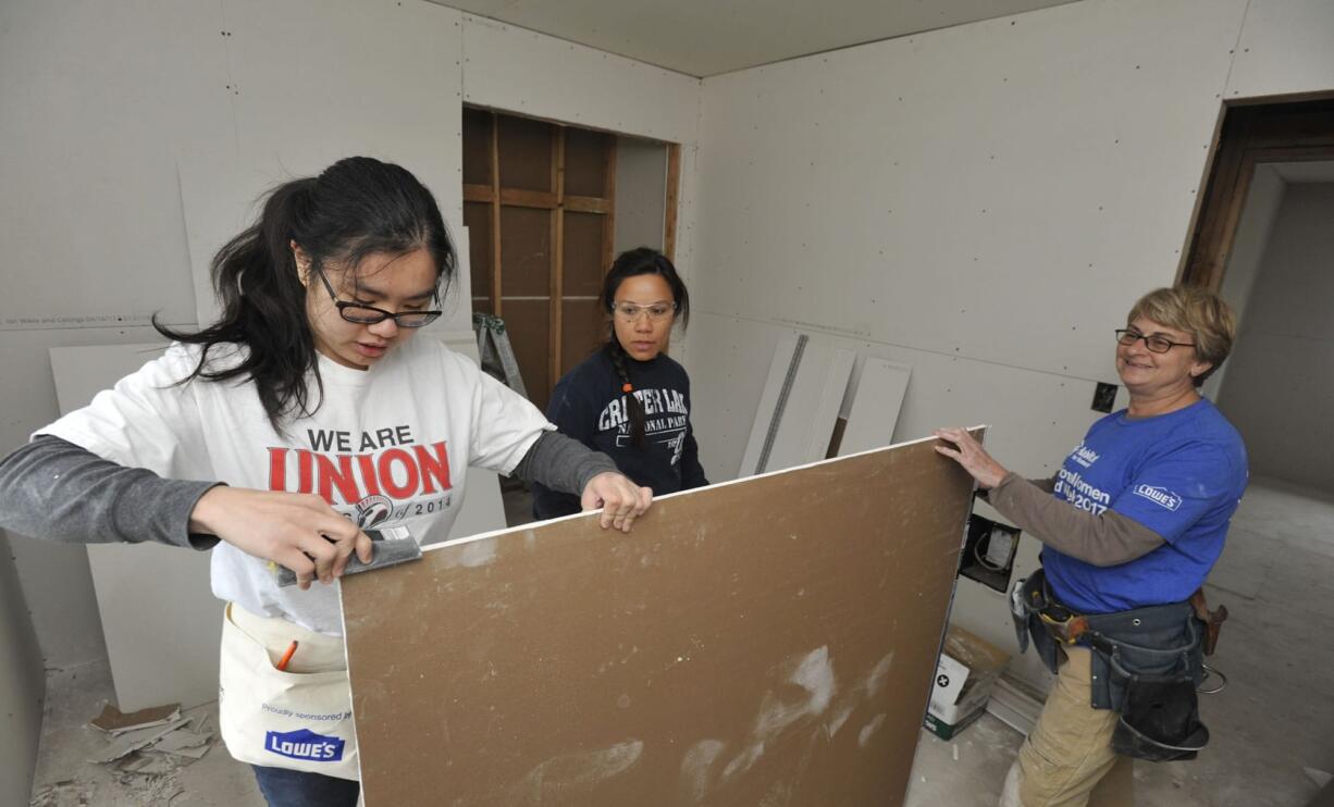 Volunteers for Evergreen Habitat for humanity, from left, Christy Tan, Marianne Gaviola and Terri Brouillet, hang sheetrock in the home of Crystal Helsel at the McKibbin Commons subdivision in Vancouver in May 13.