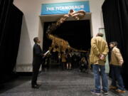 File-This Jan. 14, 2016, file photo shows visitors to the American Museum of Natural History examining a replica of a 122-foot-long dinosaur on display at the American Museum of Natural History in New York. A study proclaims a newly named species the heavyweight champion of all dinosaurs. The plant-eating giant is the largest of a group of dinosaurs called titanosaurs (tye-TAN’-u-sawr). At 76 tons (69 metric tons), the behemoth was as heavy as a space shuttle. A scientific paper released Tuesday, Aug. 8, 2017, describes and dates the fossils found in southern Argentina in 2012. A skeleton of the dinosaur is already on display at the American Museum of Natural History in New York.