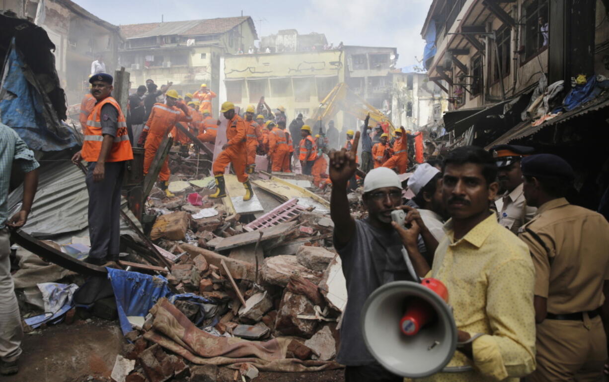 A rescue worker makes an announcement on a loudspeaker at the site of a building collapse in Mumbai, India, on Thursday. A five-story building collapsed Thursday in Mumbai, Indian’s financial capital, after torrential rains lashed western India.