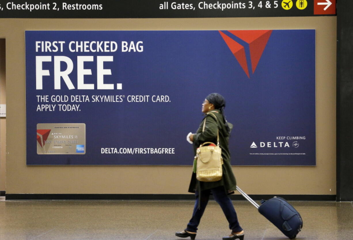 FILE - In this Tuesday, March 24, 2015, file photo, a traveler walks past a sign advertising a Delta Air Lines credit card at Seattle-Tacoma International Airport in SeaTac, Wash. Airline loyalty programs are losing much of their allure even for frequent flyers, and the rules for navigating the system have changed. The biggest bang for your buck comes from signing up for the right credit card. Even if you make purchases with another card, consider getting the card of the airline you usually fly to enjoy benefits such as priority boarding and free bag-checking, even on so-called basic economy tickets. If you check a bag a few times a year, you will more than offset the annual fee.