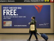 FILE - In this Tuesday, March 24, 2015, file photo, a traveler walks past a sign advertising a Delta Air Lines credit card at Seattle-Tacoma International Airport in SeaTac, Wash. Airline loyalty programs are losing much of their allure even for frequent flyers, and the rules for navigating the system have changed. The biggest bang for your buck comes from signing up for the right credit card. Even if you make purchases with another card, consider getting the card of the airline you usually fly to enjoy benefits such as priority boarding and free bag-checking, even on so-called basic economy tickets. If you check a bag a few times a year, you will more than offset the annual fee.