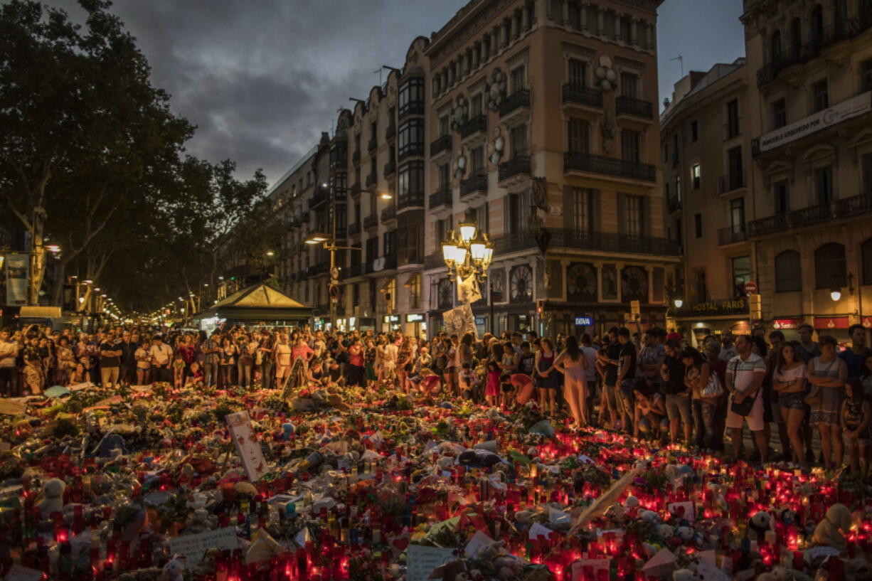 People stand next to candles and flowers placed on the ground, after a terror attack that left many killed and wounded in Barcelona, Spain, on Monday. The lone fugitive from the Spanish cell that killed 15 people in and near Barcelona was shot to death Monday after he flashed what turned out to be a fake suicide belt at two troopers who confronted him in a vineyard just outside the city he terrorized, authorities said.