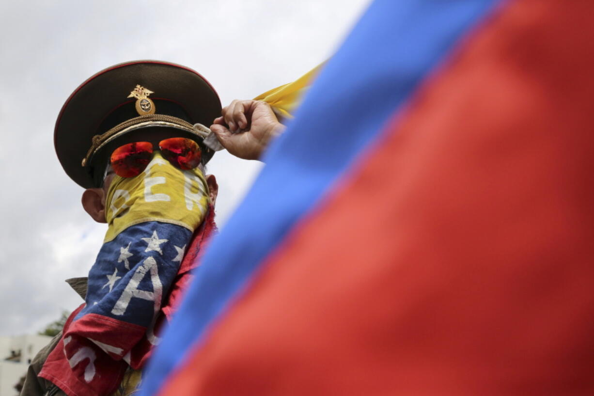 An anti-government demonstrator wearing a Russian military hat, and his face covered with a Venezuelan flag, protests the government of Venezuela’s President Nicolas Maduro in Caracas, Venezuela, Sunday. Venezuelan ruling party chief Diosdado Cabello said the military squashed a “terrorist” attack at a military base on Sunday, shortly after a small group of men dressed in military fatigues released a video declaring themselves in rebellion.