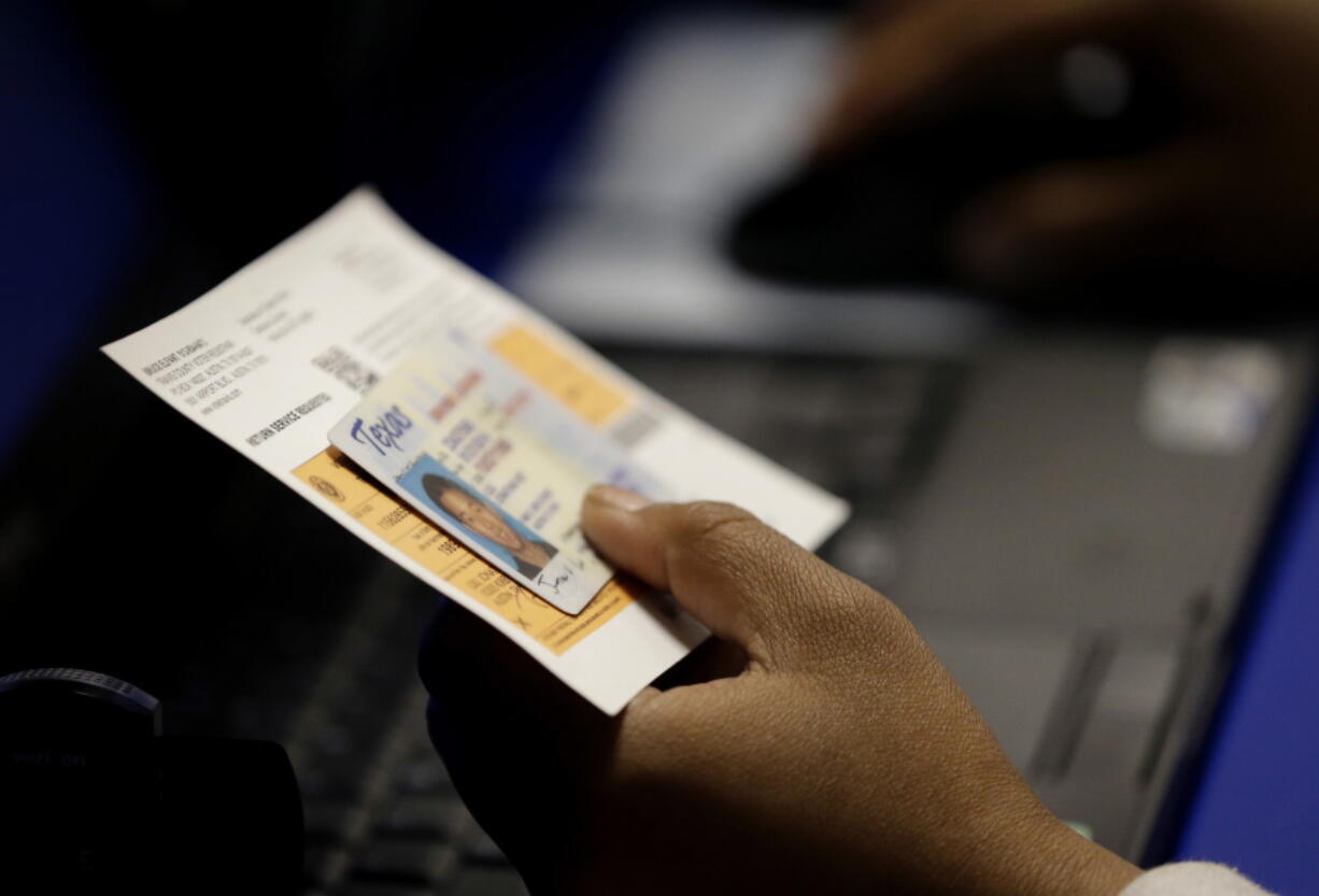 FILE - In this Feb. 26, 2014 file photo, an election official checks a voter’s photo identification at an early voting polling site in Austin, Texas. A federal judge Wednesday, Aug. 23, 2017, again threw out Texas’ voter ID requirements that she previously compared to a “poll tax” on minorities, dealing another court setback to state Republican leaders over voting rights.