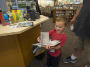 Connor Jackson, 5, of Vancouver flips through a book he checked out Friday after he and his dad, Mike, visited the Washougal Community Library. A new library would include a children’s area. Staffers now must roll bookcases out of the way for story times.