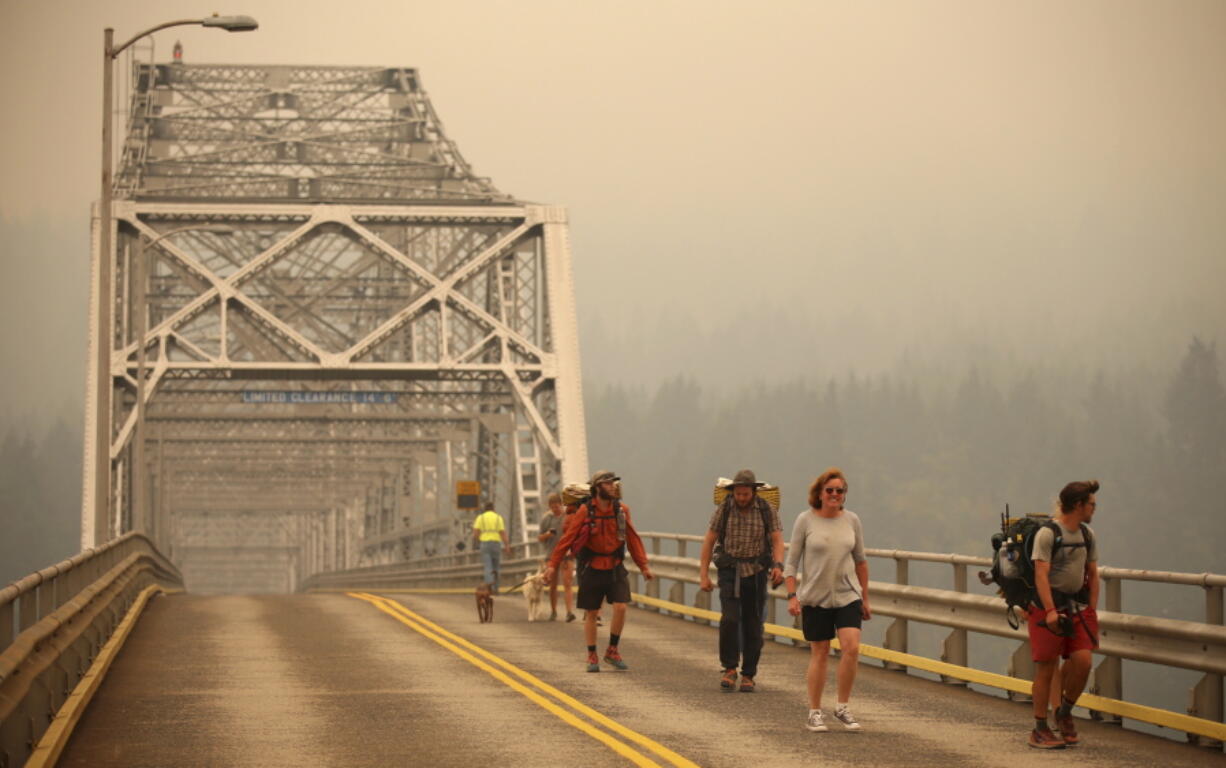 Pedestrians walk off the Bridge of the Gods, which spans the Columbia River between Washington and Oregon states, as smoke from the Eagle Creek wildfire obscures the Oregon hills in the background near Stevenson on Sept. 6, 2017. (AP Photo/Randy L.