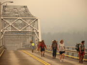 Pedestrians walk off the Bridge of the Gods, which spans the Columbia River between Washington and Oregon states, as smoke from the Eagle Creek wildfire obscures the Oregon hills in the background near Stevenson on Sept. 6, 2017. (AP Photo/Randy L.