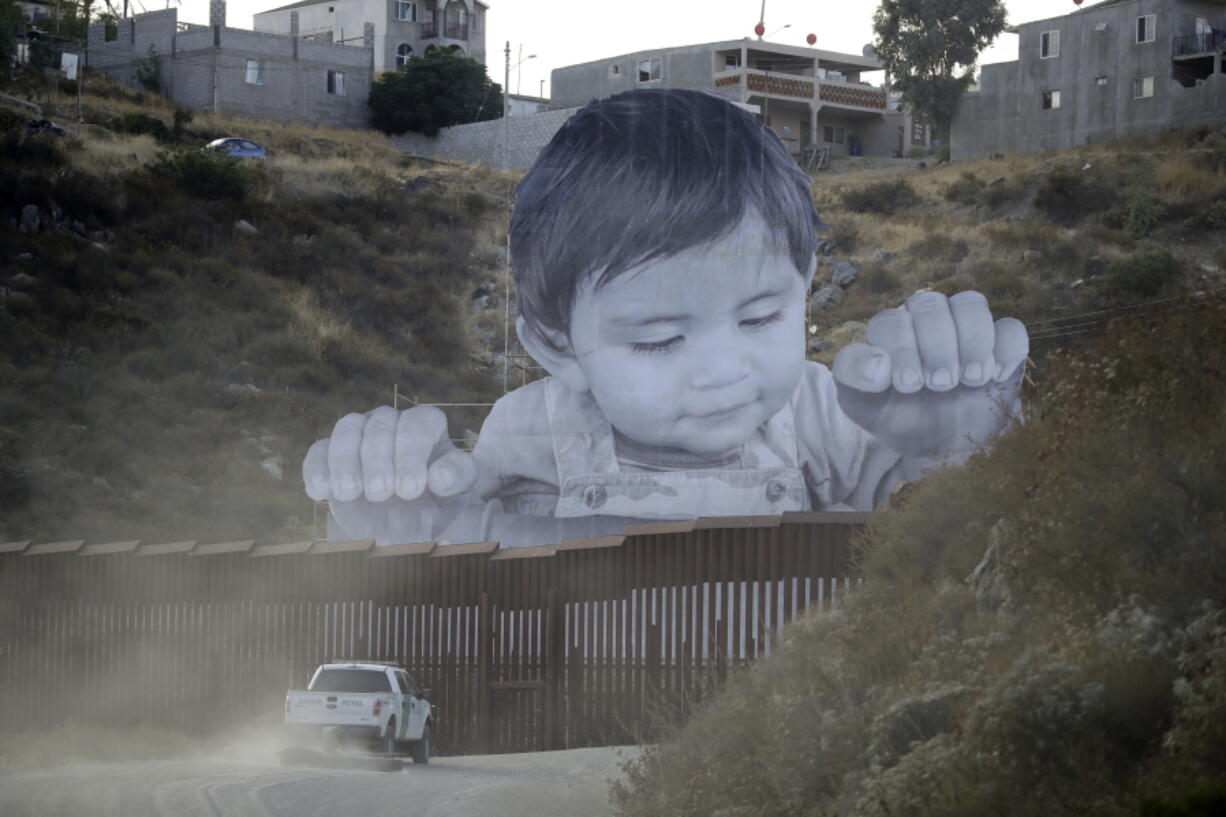 A Border Patrol vehicle drives in front of a mural in Tecate, Mexico, just beyond a border structure Friday, Sept. 8, 2017, in Tecate, Calif. A French artist aiming to prompt discussions about immigration erected a 65-foot-tall cut-out photo of a Mexican boy, pasting it to scaffolding built in Mexico. The image overlooks a section of wall on the California border and will be there for a month.