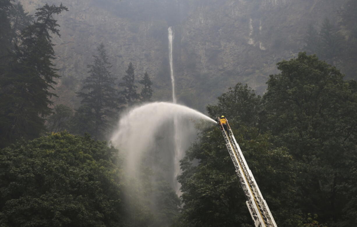 A firefighter maintains a spray of water on the trees around Multnomah Falls on Wednesday as the Eagle Creek Fire continues to burn east of Troutdale, Ore.