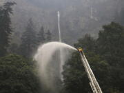 A firefighter maintains a spray of water on the trees around Multnomah Falls on Wednesday as the Eagle Creek Fire continues to burn east of Troutdale, Ore.