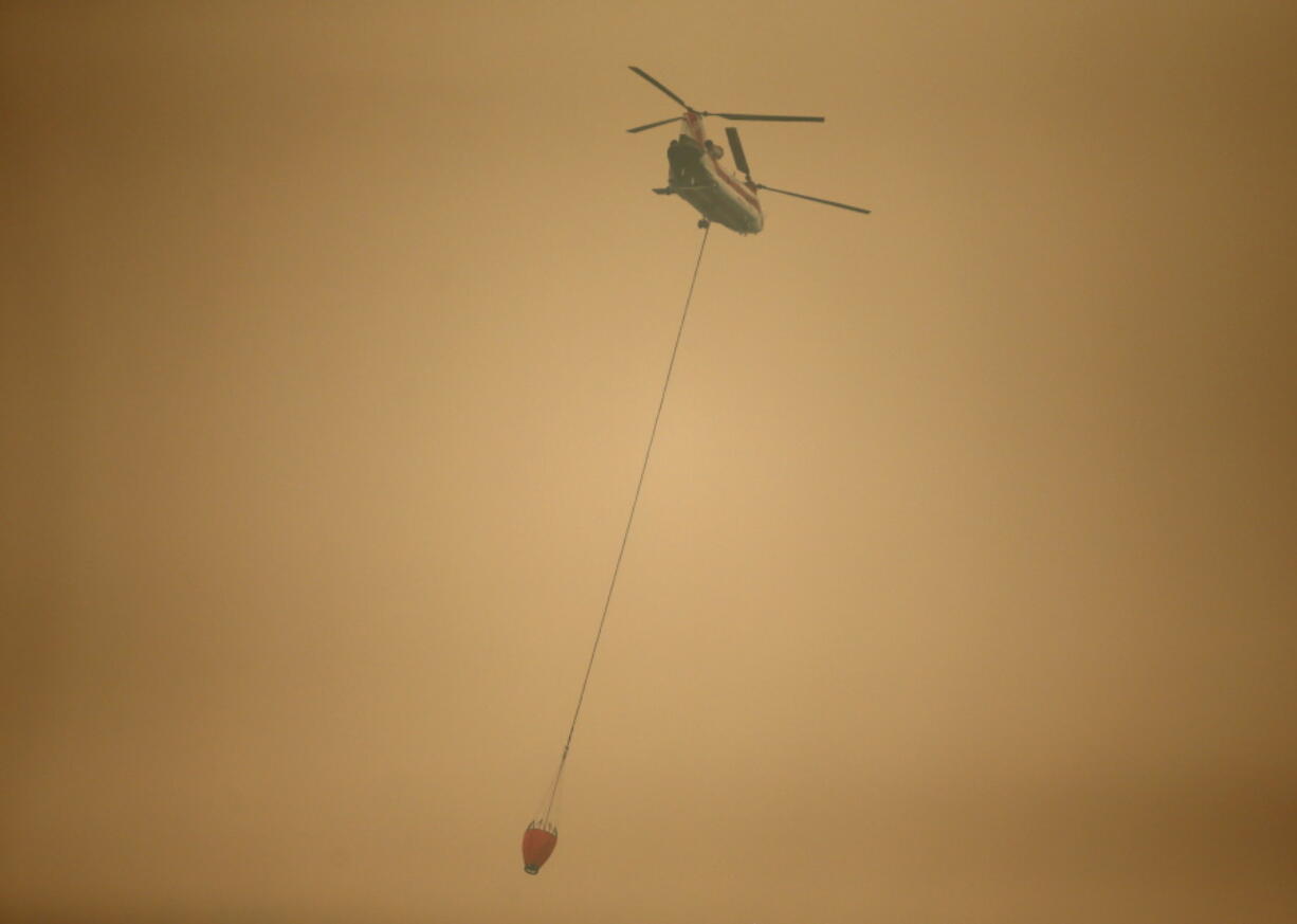 A helicopter with a water bucket flies through dense smoke near Stevenson, Wash., Wednesday, Sept. 6, 2017, as it works to battle the Eagle Creek wildfire on the Oregon side of the Columbia River Gorge. (AP Photo/Randy L.