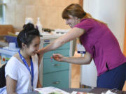 Nicole Nguyen, a volunteer at Legacy Salmon Creek Medical Center, left, receives a flu shot from registered nurse Lindsey Wreden on Friday. Wreden has for several weeks pushed a cart around the hospital, vaccinating employees and volunteers against the seasonal flu.