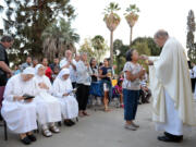 Bishop Armando X. Ochoa of the Roman Catholic Diocese of Fresno, Calif., gives communion to participants during a mass at Kearney Park as part of the Roman Catholic Diocese of Fresno’s 50th anniversary conducted through their mobile chapel .