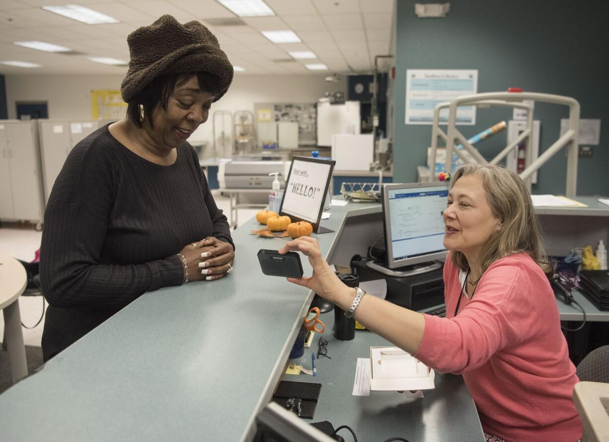 Barbara Alderman, the grandmother of two students at Discovery Middle School, left, looks at a Wi-Fi hot spot device she's receiving from Angela Vahsholtz-Andersen, a teacher librarian at Discovery Middle School, in the library of the school on Wednesday. As districts are giving iPads to students, they're discovering that low-income students aren't able to make the most of these devices if they don't have Internet at home. On Wednesday, parents came to Discovery Middle School to pick up Wi-Fi hotspot devices provided by a grant Vancouver Public Schools received this year.