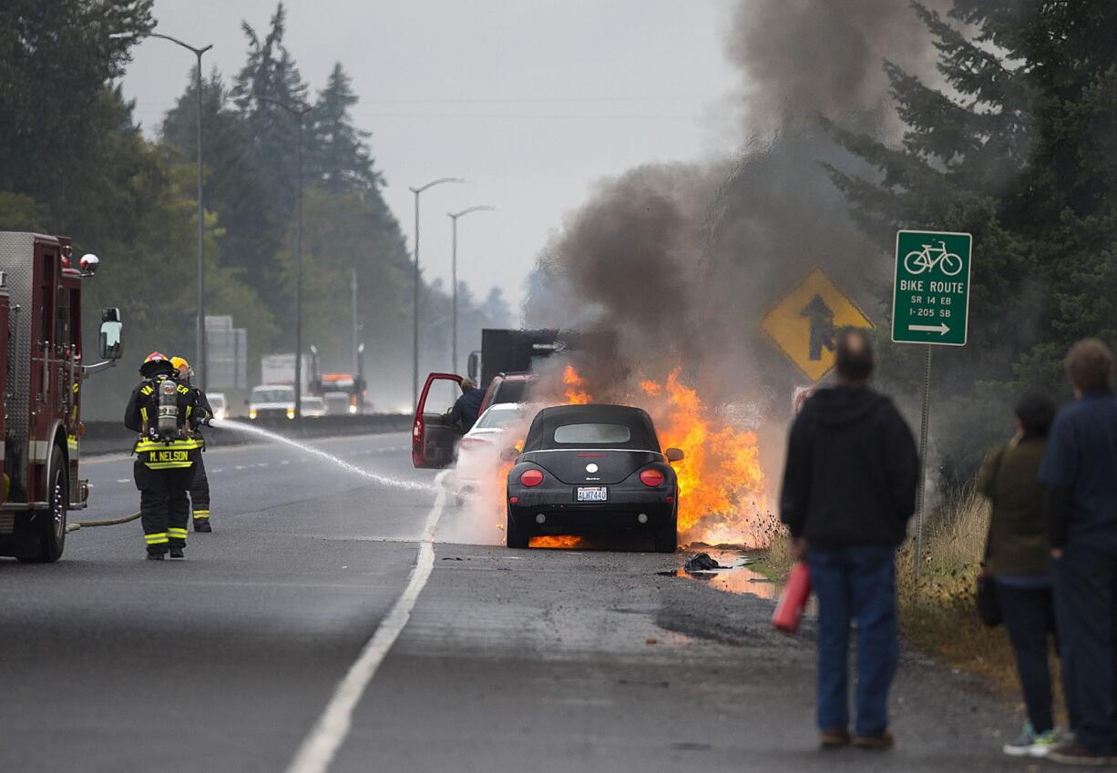 Firefighters extinguish a car on fire along State Highway 14 about a mile east of the Lieser Road exit as people look on Wednesday morning, Oct. 18, 2017. Traffic traveling in the westbound lane was backed up and routed around the scene. No injuries were reported.