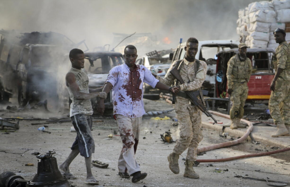 A Somali soldier helps a civilian who was wounded in a blast in the capital of Mogadishu, Somalia, Saturday, Oct. 14, 2017. A huge explosion from a truck bomb has killed at least 20 people in Somalia's capital, police said Saturday, as shaken residents called it the most powerful blast they'd heard in years.