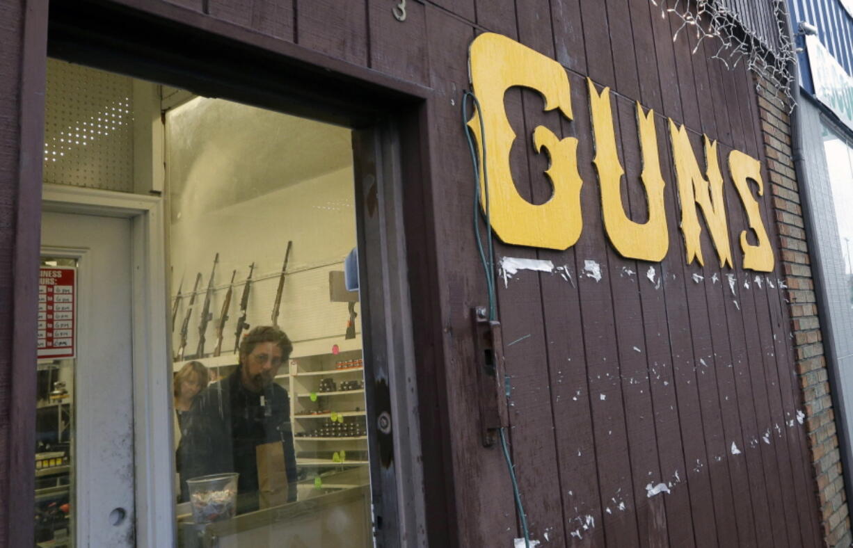 FILE - This Dec. 19, 2012 file photo show rifles line a wall above in front of people standing in a gun shop in Seattle. The slaying of five dozen people at a Las Vegas music festival did little to change American opinion about the nation’s gun laws, and the country is divided over whether restricting firearms would reduce the number of such mass shootings or homicides, according to a new poll from The Associated Press-NORC Center for Public Affairs Research.