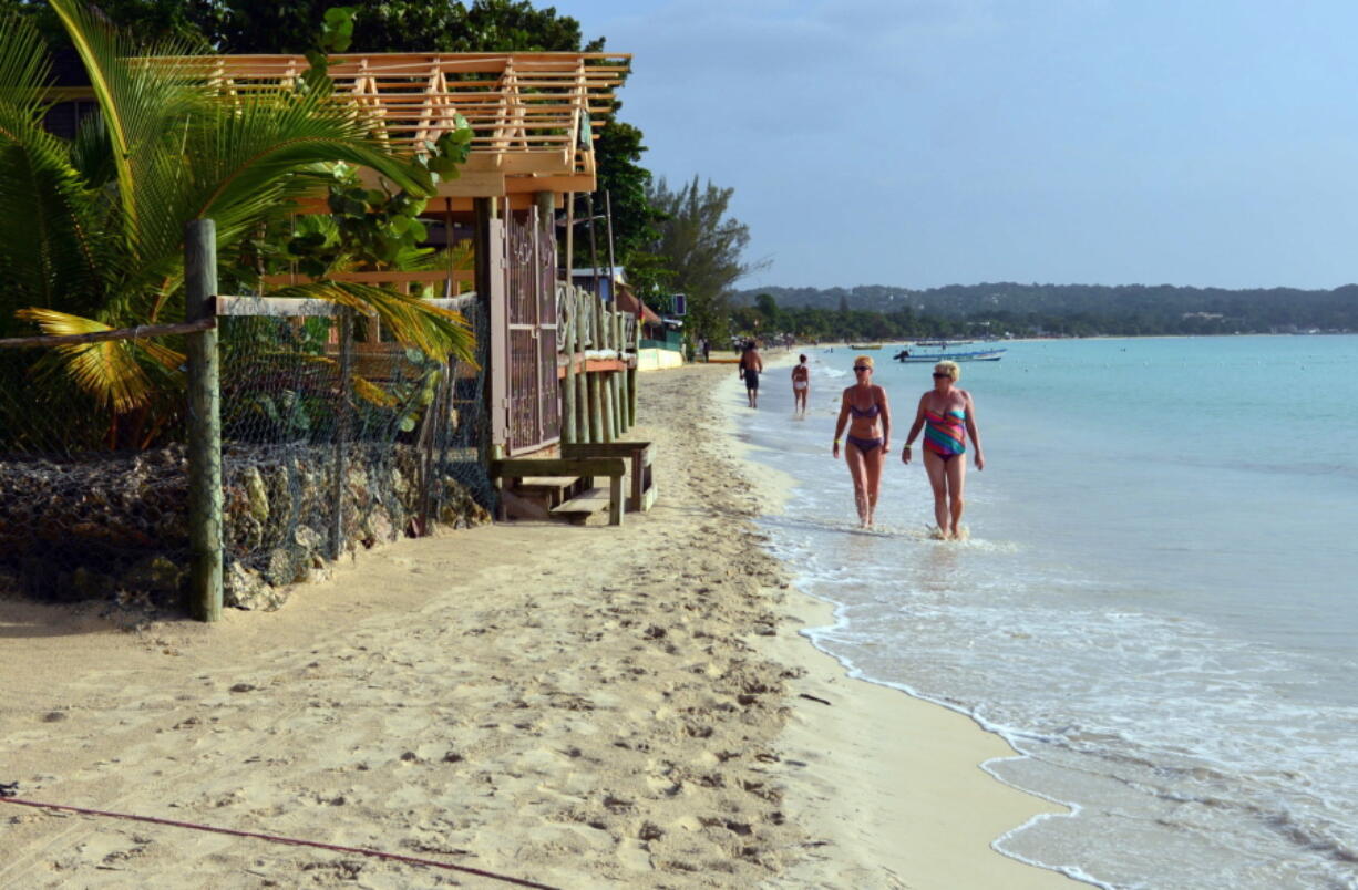 FILE - In this Sept. 14, 2014, file photo, sunbathers walk along a badly eroding patch of resort-lined crescent beach in Negril in western Jamaica. While some islands in the Caribbean were hard-hit by this season’s hurricanes, others were relatively unscathed and are open for business as usual.