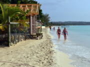 FILE - In this Sept. 14, 2014, file photo, sunbathers walk along a badly eroding patch of resort-lined crescent beach in Negril in western Jamaica. While some islands in the Caribbean were hard-hit by this season’s hurricanes, others were relatively unscathed and are open for business as usual.