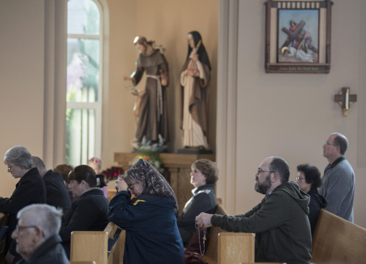 People bow their heads in prayer before the start of All Saints’ Day Mass at Holy Redeemer Catholic Parish in east Vancouver. In the background are statues of St. Francis and St. Clare.