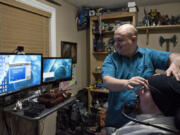 Dustin Troupe helps his friend Brandon Powell adjust an EEG headband so he can play “World of Warcraft” at his home in Vancouver on Nov. 10. With an EEG sensor headband and a program called Brainfingers, Powell’s facial muscles, eye movements, and brainwaves are used to control the movement and click of a mouse. Powell became paralyzed from the shoulders down after being shot in the neck by a sniper while deployed in Iraq in 2004.