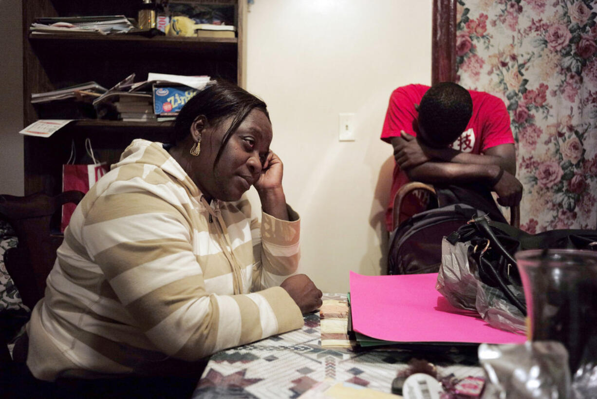 In this Wednesday, Nov. 15, 2017 photo, Marianne Jeune, left, a Haitian immigrant staying in the U.S. through the Temporary Protected Status program, sits in her Boston home while her son Amocachy Jeune, right, stands nearby. She has worked a variety of jobs caring for the elderly, and lost her home in Haiti in the 2010 earthquake. The healthcare industry is concerned about the potential loss of thousands of workers from Haiti as President Donald Trump weighs whether to extend Temporary Protected Status for some 58,000 Haitians that have lived in the country since at least 2010.