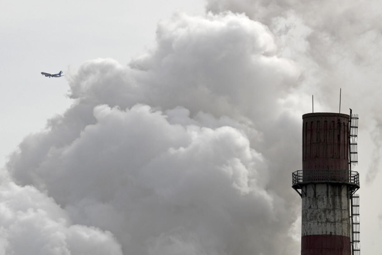 A passenger airplane flies behind steam and white smoke emitted from a coal-fired power plant in Beijing. On Monday, Nov. 13, 2017, scientists projected that global carbon pollution has risen in 2017 after three straight years when the heat-trapping gas didn’t go up at all.