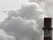 A passenger airplane flies behind steam and white smoke emitted from a coal-fired power plant in Beijing. On Monday, Nov. 13, 2017, scientists projected that global carbon pollution has risen in 2017 after three straight years when the heat-trapping gas didn’t go up at all.