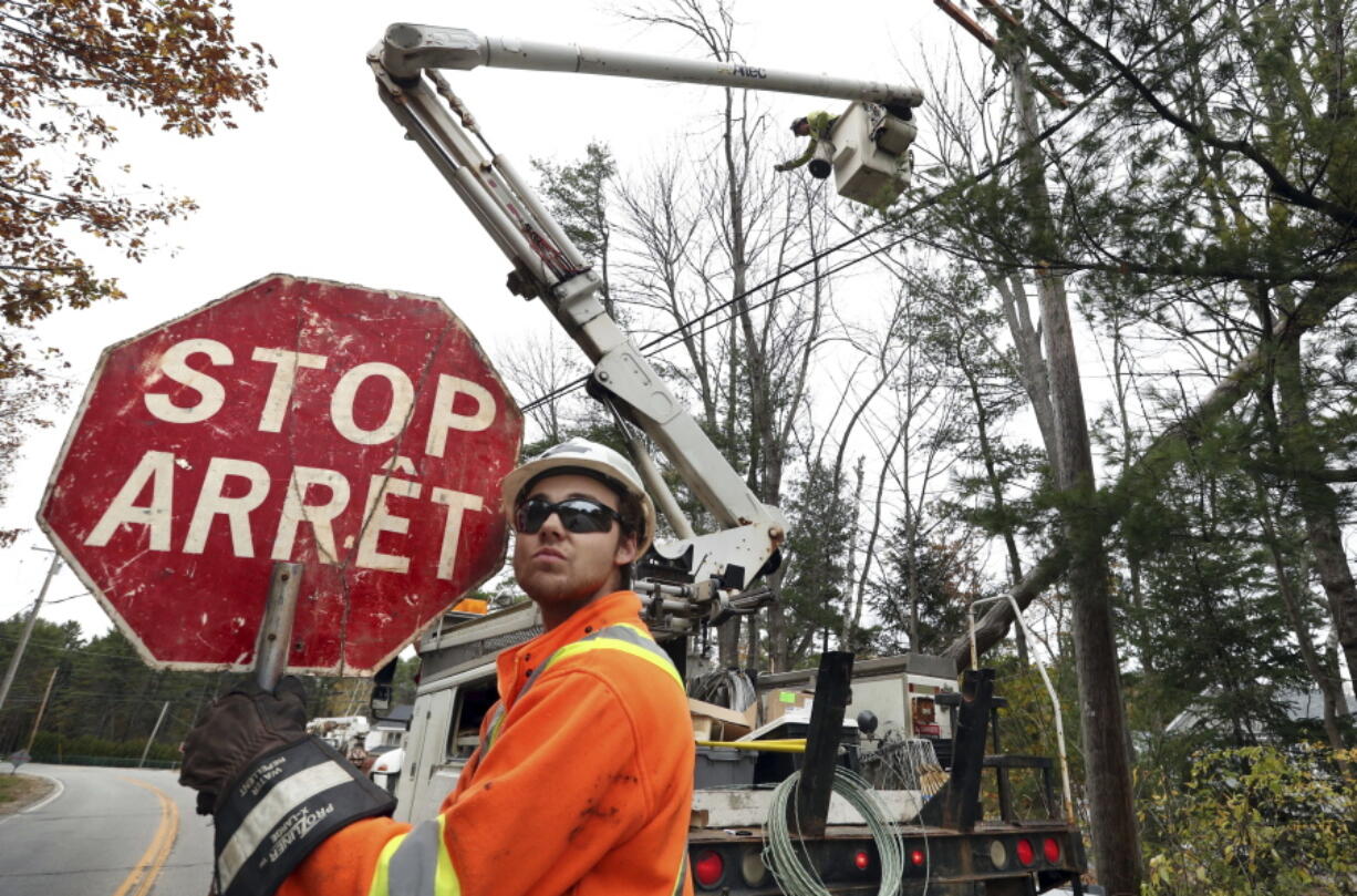 Canadian lineman Noah Clowater holds a bilingual stop sign while directing traffic while his coworkers restore power Wednesday in Yarmouth, Maine. The New Brunswick, Canada, crew were among the hundreds of line and tree workers from as far away as Illinois, Kentucky, Ohio and West Virginia that have come to Maine following Monday’s storm that knocked out power to nearly two-thirds of the state. (AP Photo/Robert F.