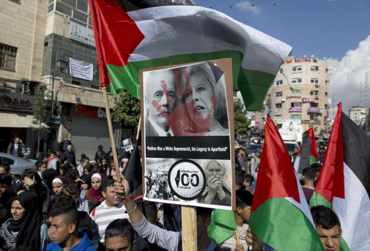 Protesters wave Palestinian flags and carry a defaced photo of UK Prime Minister Theresa May, and Arthur Balfour, on the 100th anniversary of the Balfour Declaration, in Ramallah, Thursday, Nov. 2, 2017. Thousands of Palestinians have taken to the streets in protest across the West Bank marking a century since the Balfour Declaration, Britain's promise to Zionists to create a Jewish home in what is now Israel.