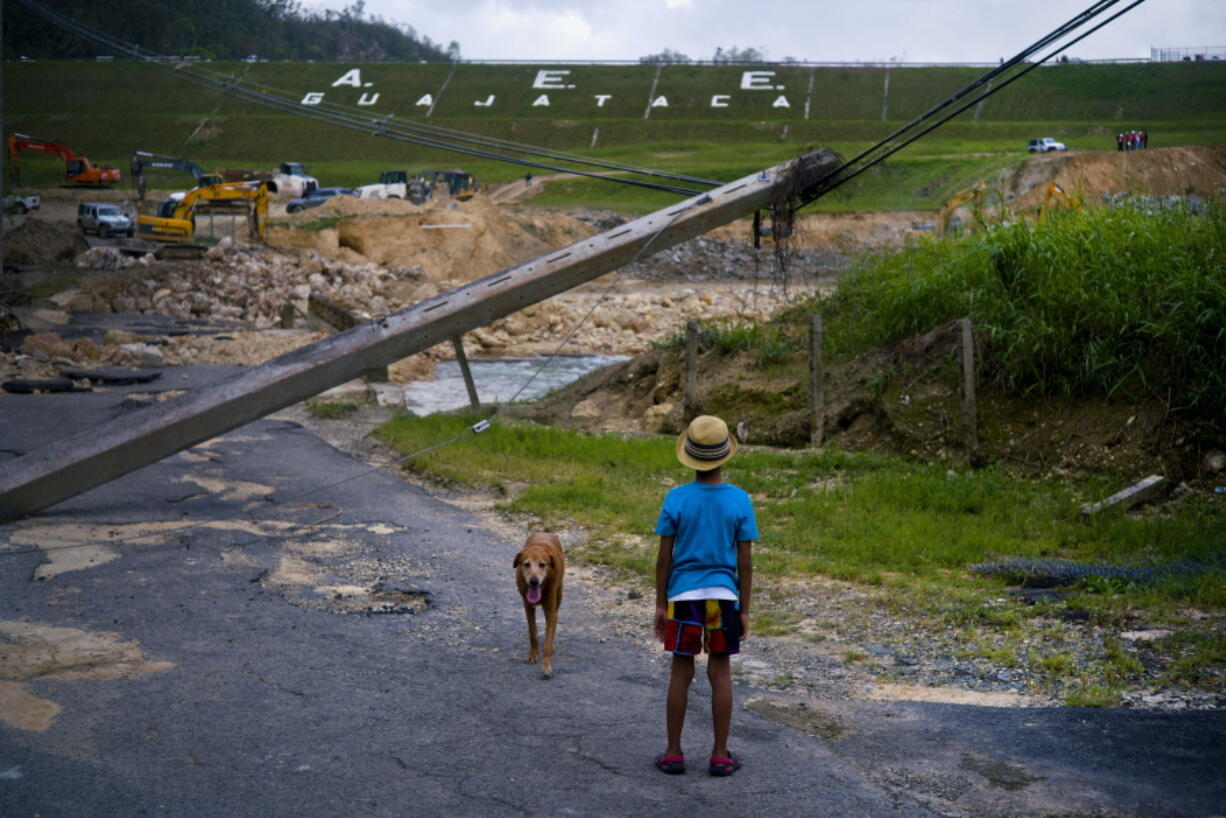 FILE - In this Oct. 17, 2017 file photo, a boy accompanied by his dog watches the repairs of Guajataca Dam, which cracked during the passage of Hurricane Maria, in Quebradillas, Puerto Rico. Experts said on Thursday, Nov. 16, 2017, that Puerto Rico could face nearly two decades of further economic stagnation and a steep drop in population as a result of Maria.