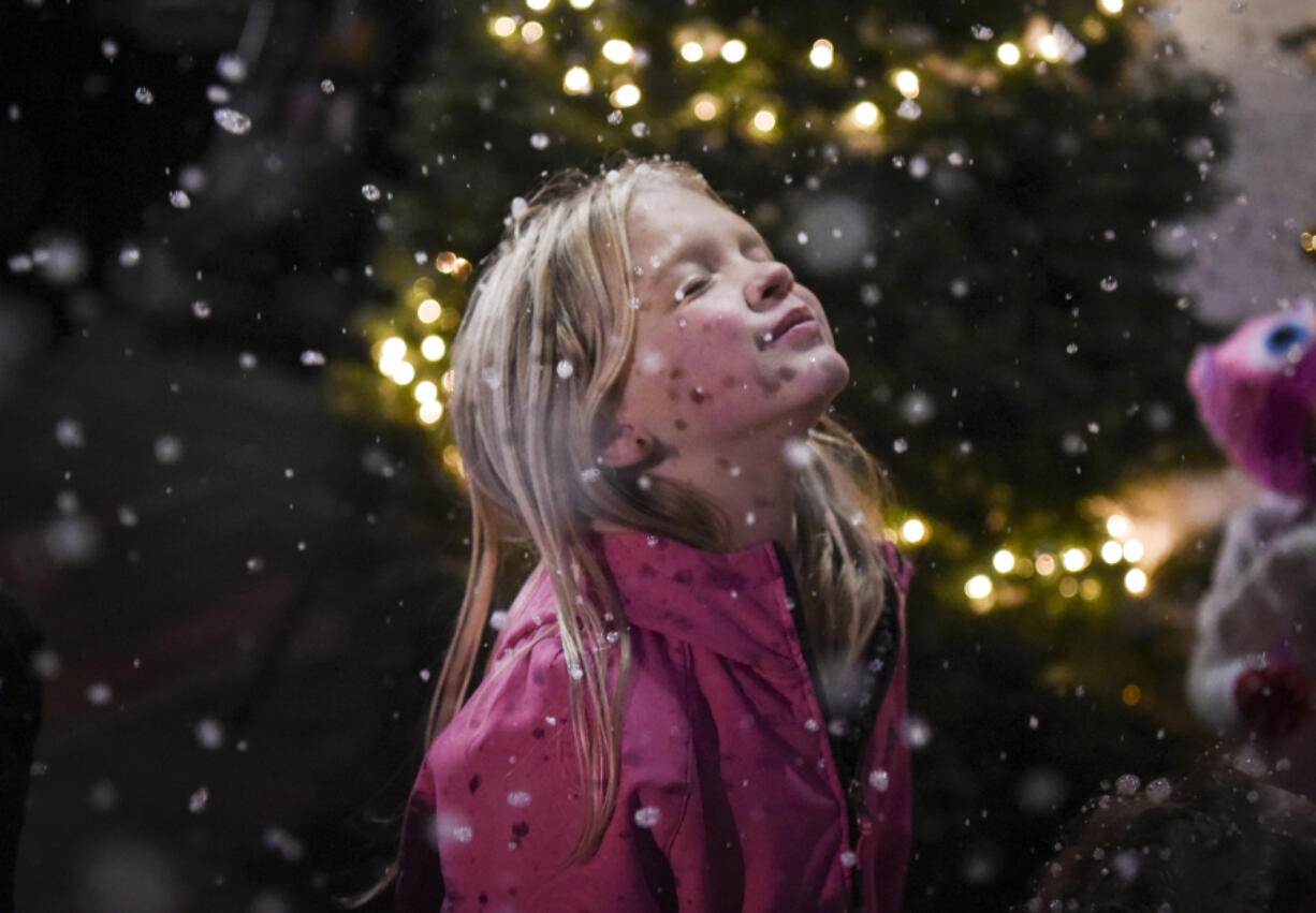 Serena Brown, 8, closes her eyes as snowflakes from a snow machine fall on her face Friday at Activate Church’s sixth annual Christmas at the Park in Esther Short Park. Below: Yesenia Alcazar, left, helps her children, Marley Compos, 2, left, and Damian Campos, 9, decorate Christmas cookies.